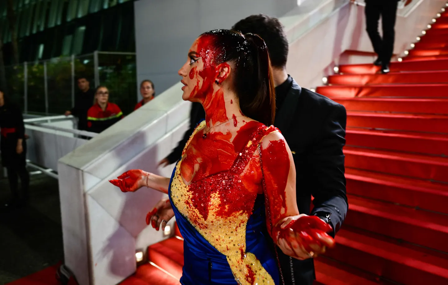 Meeleavaldaja, kes kandis kollases ja sinises toonides kleiti, kallas end filmifestivali punasel vaibal võltsverega üle.
