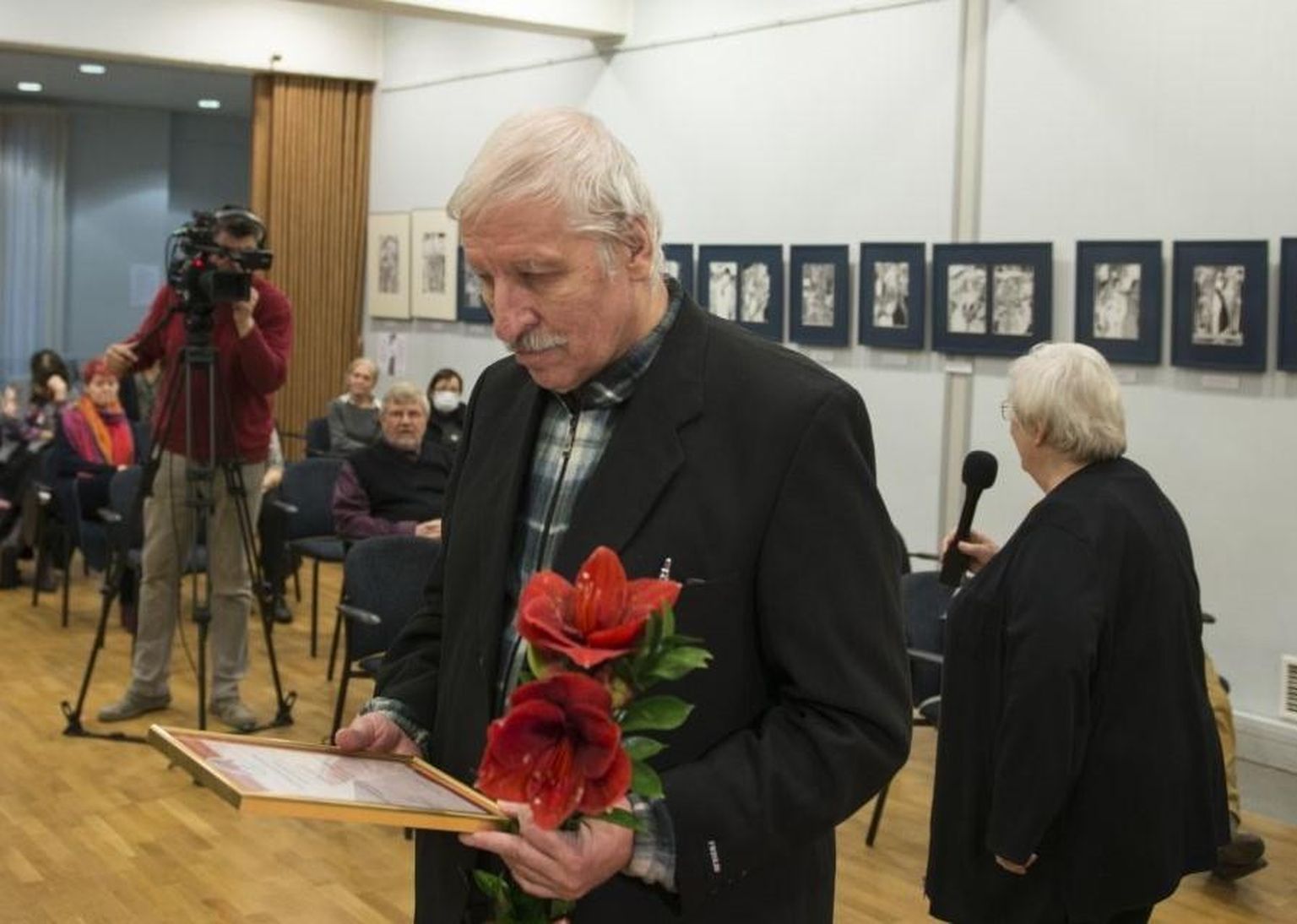 Aivar Kull uurib kirjandusmuuseumi saalis preemiaga kaasas käinud tunnistust, mis on raamitud ja klaasi alla pandud. Paremal kõneleb Marju Lauristin.