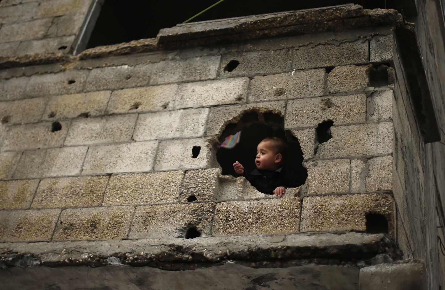Palestiina poisike vaatab välja Gazas asuva kodumaja seinas olevast august, mis väidetavalt tekkis Iisraeli tulistatud kahurikuulist juulis-augustis 2014.