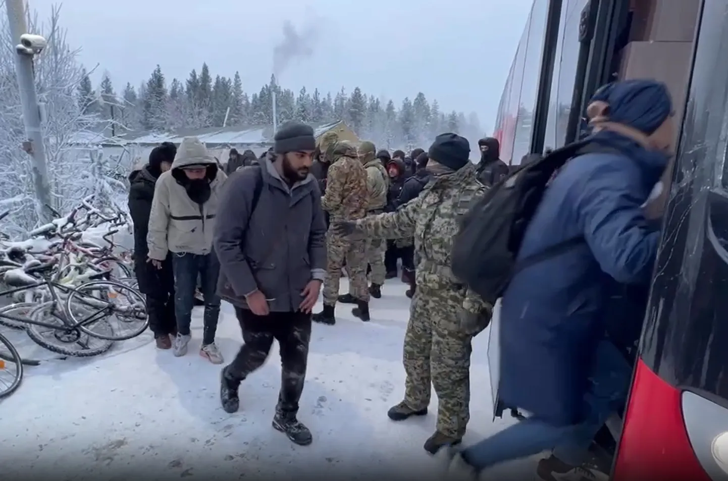 Сотрудники ФСБ контролируют загрузку мигрантов в автобус около закрытого финского КПП на юге Мурманской области, чтобы переехать на север региона, где погранпереход пока еще открыт, 24 ноября 2023 года.