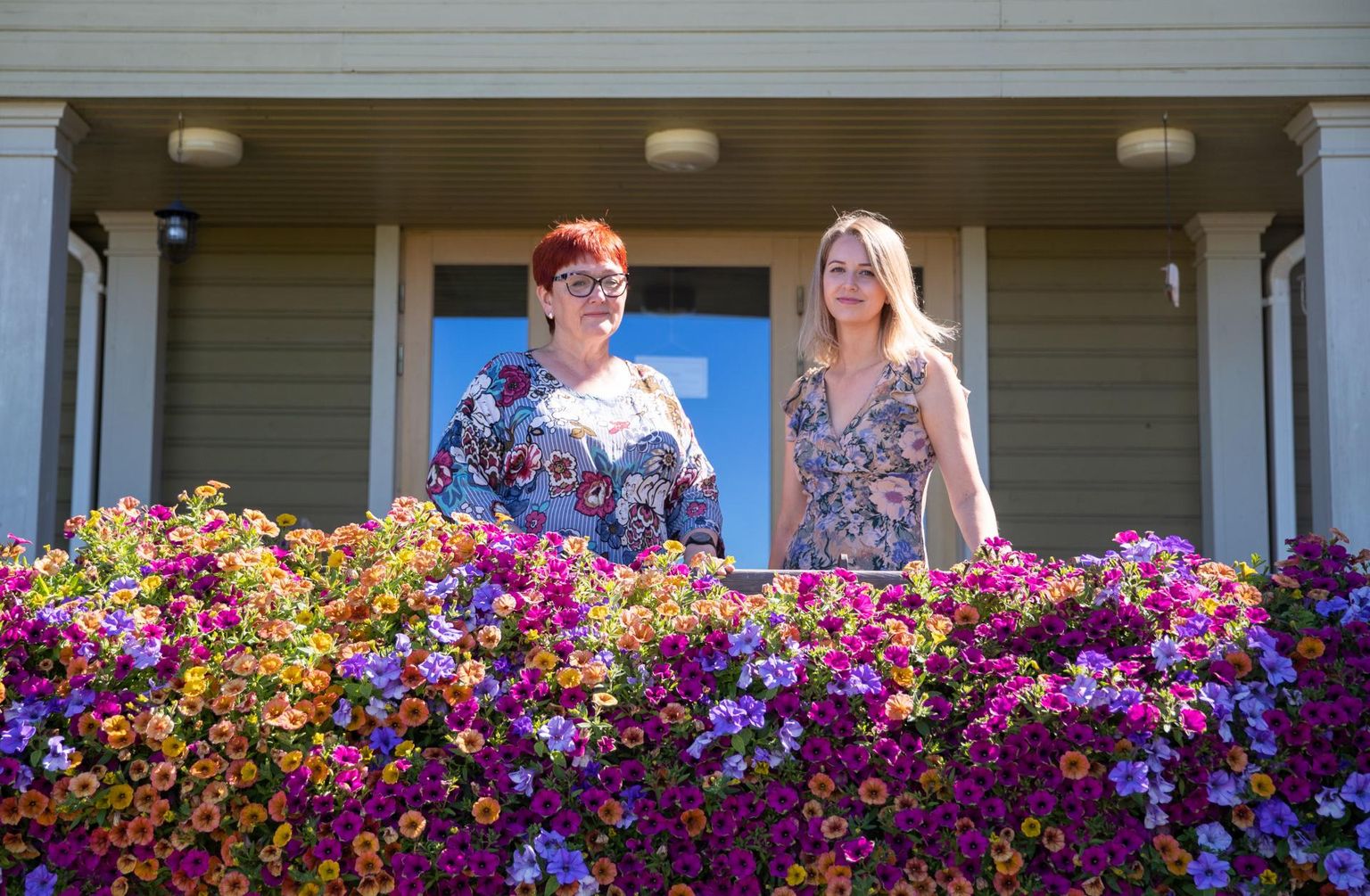 Altmõisa pererahvas külalistemaja-suvekohviku lilleklumpidega ehitud peasissekäigu ees: ema ja tütar, peakokk Meeli Lokk ja juhataja Anna Regina Kabral.
 