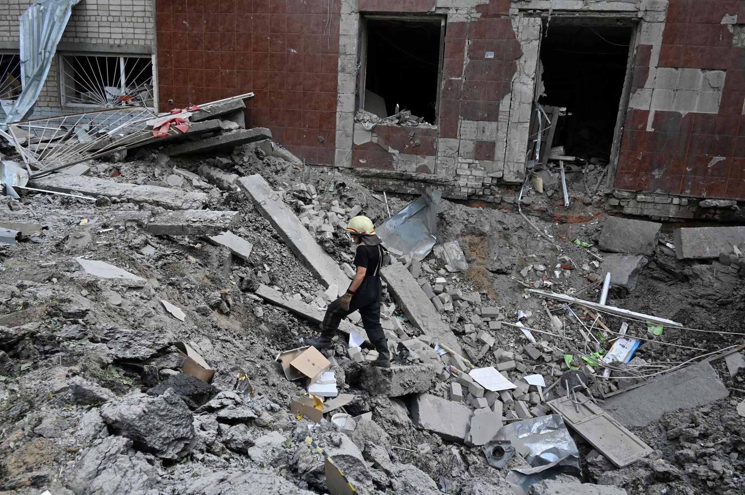 A rescuer stands in a crater in the ruins of a school building, partially destroyed by two rockets in the Ukrainian city of Kharkiv on June 28, 2022. (Photo by SERGEY BOBOK / AFP)